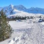 Wejście na zaśnieżoną Halę Gąsienicową, w oddali turyści, drewniane chatki, w tym Betlejemka oraz zaśnieżone tatrzańskie szczyty - między innymi Kościelec