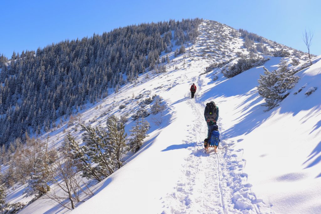 Zima, podejście niebieskim szlakiem w kierunku Przełęczy między Kopami, turysta ciągnący dziecko na sankach, widok na szczyt noszący nazwę Wielka Królowa Kopa