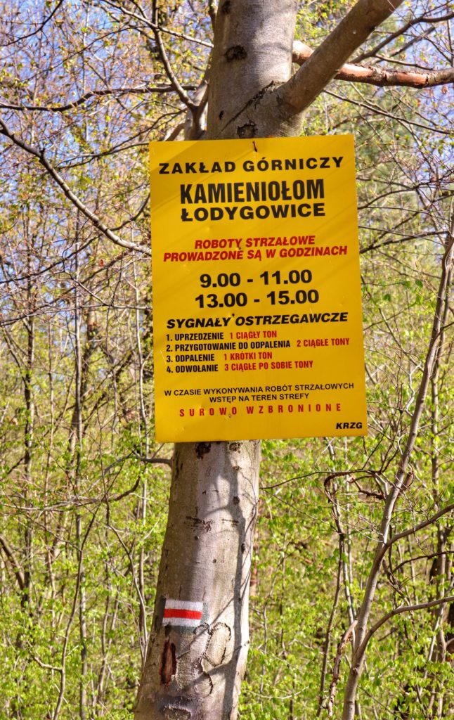 Żółta tablica Zakładu Górniczego ostrzegająca o robotach strzałowych, Kamieniołom Łodygowice na czerwonym szlaku na Magurkę