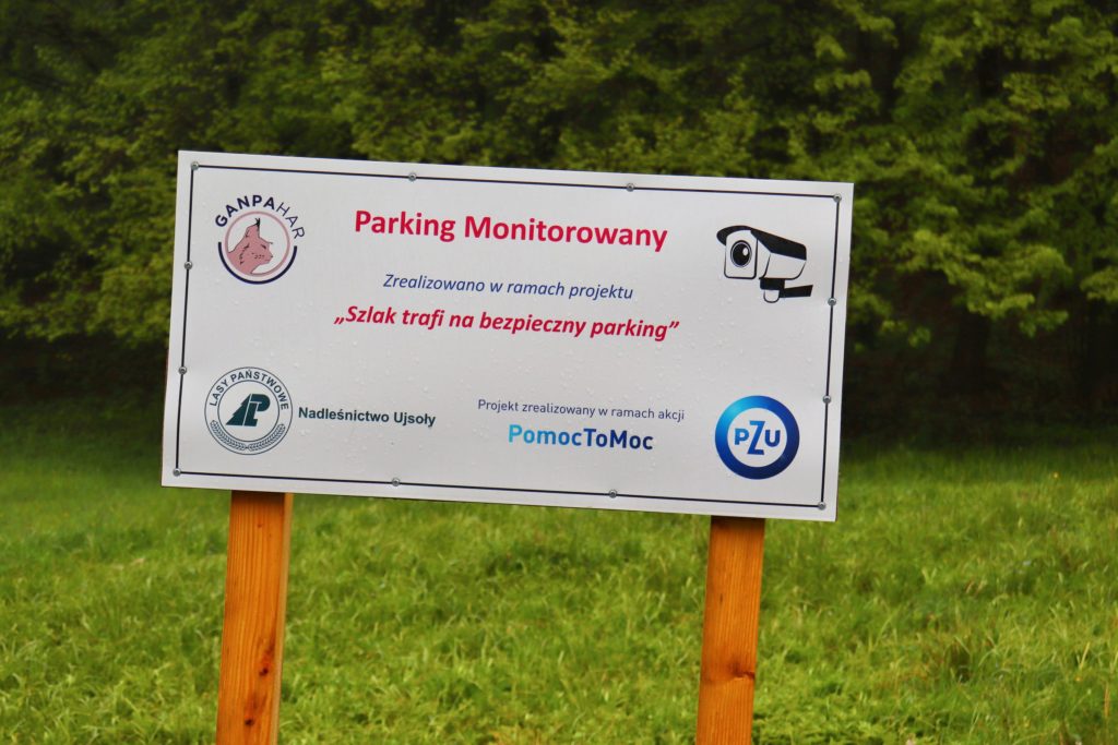 Biała tablica z napisem Parking monitorowany, zielony szlak na Bendoszkę Wielką