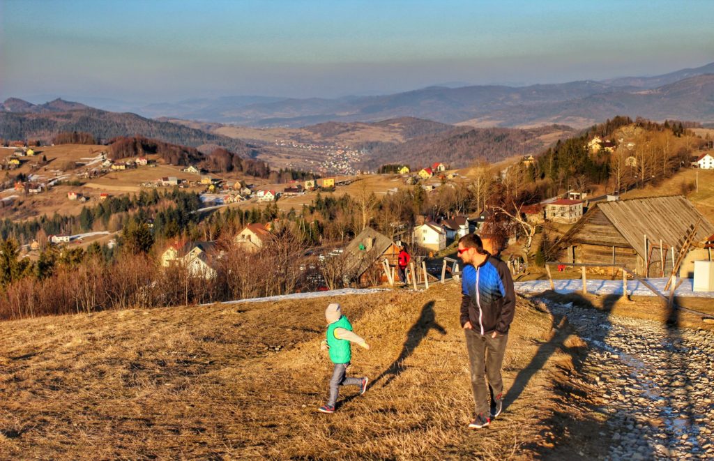 Dziecko biegnące w stronę szczytu Ochodzita wraz z tatą, piękny krajobraz górski, w oddali domy