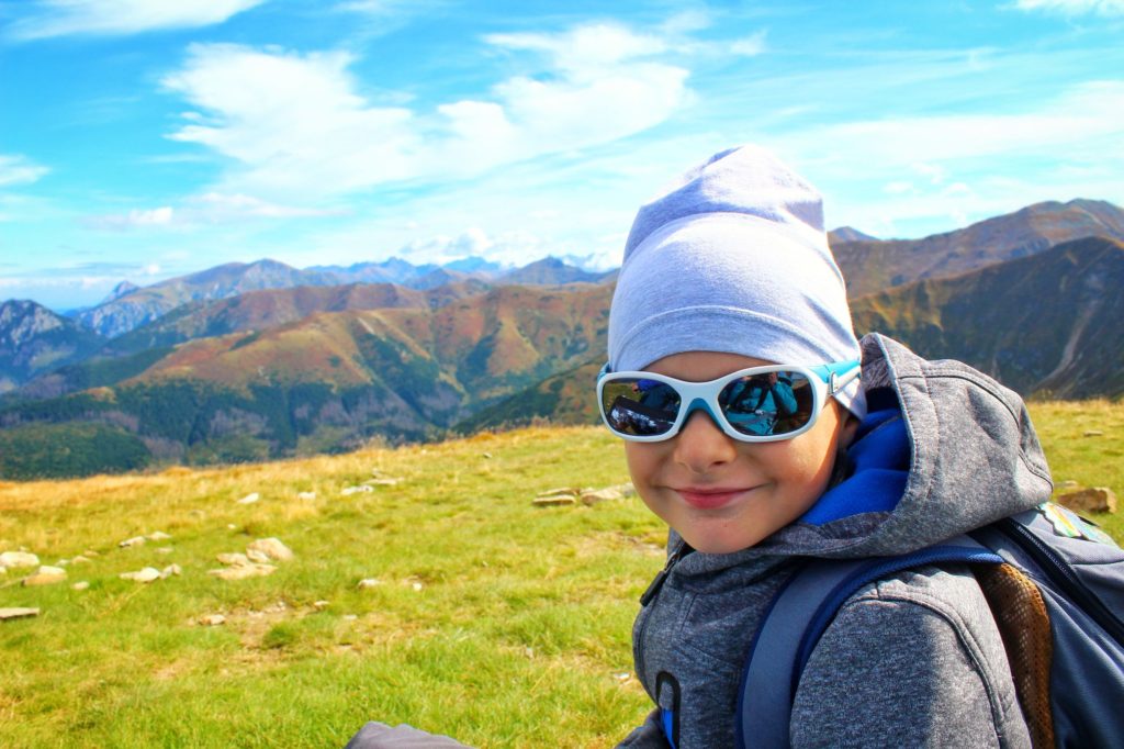 Rakoń z dzieckiem, uśmiechnięty chłopiec na szczycie Rakoń, w tle tatrzańskie szczyty