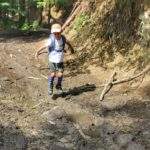 Szczęśliwe dziecko skacząc, bawiące się w błocie zalegającym na zielonym szlaku na Przegibek