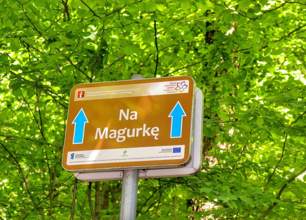 Tablica z napisem Na Magurkę na czerwonym szlakiem z Łodygowic