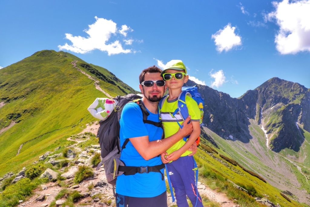 Turysta z dzieckiem na szczycie Rakoń w Tatrach Zachodnich, w oddali widoczne strome podejście w stronę Wołowca