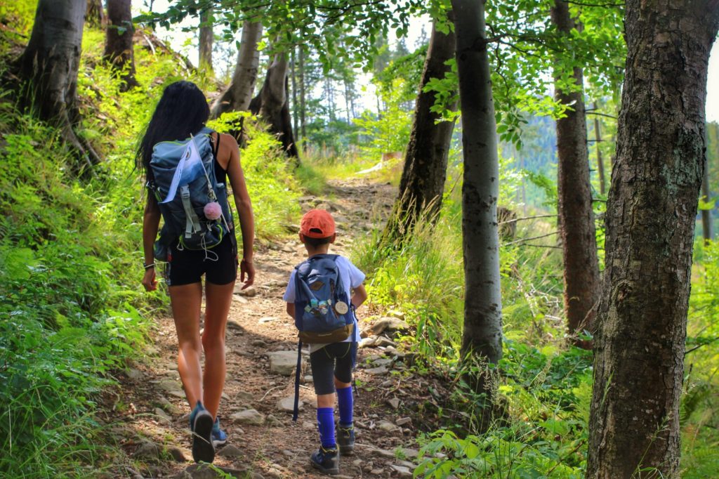 Turystka idąca z dzieckiem wąską, leśną ścieżką