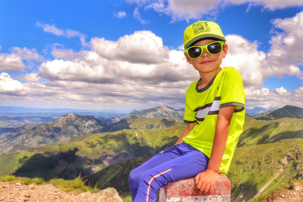 Uśmiechnięte dziecko na Wołowcu, siedzące na słupku granicznym, w tle widok na Tatry