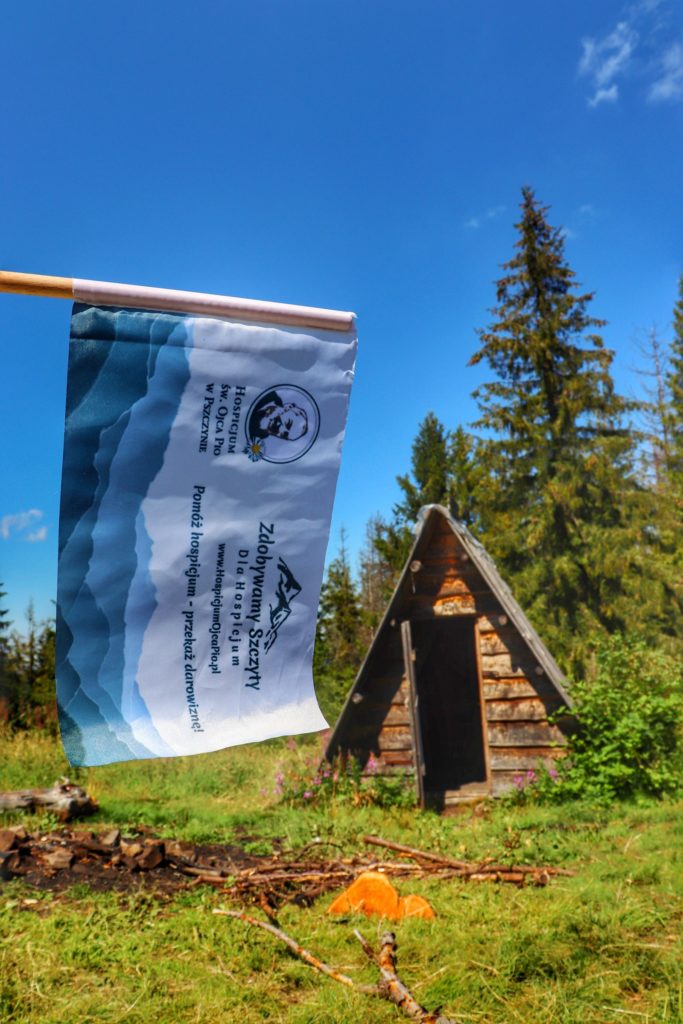 Drewniany szałas na Hali Janoszkowej, flaga akcji Zdobywamy Szczyty dla Hospicjum