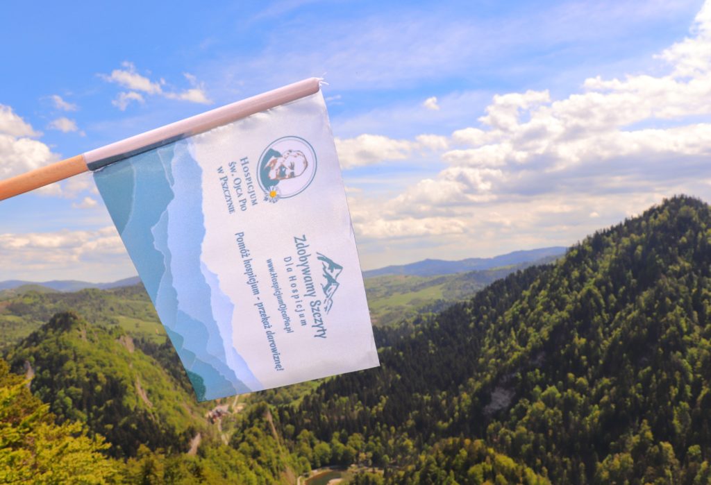 Flaga akcji Zdobywamy Szczyty dla Hospicjum, Sokolica w Pieninach, krajobraz górski, błękitne niebo z białymi obłokami