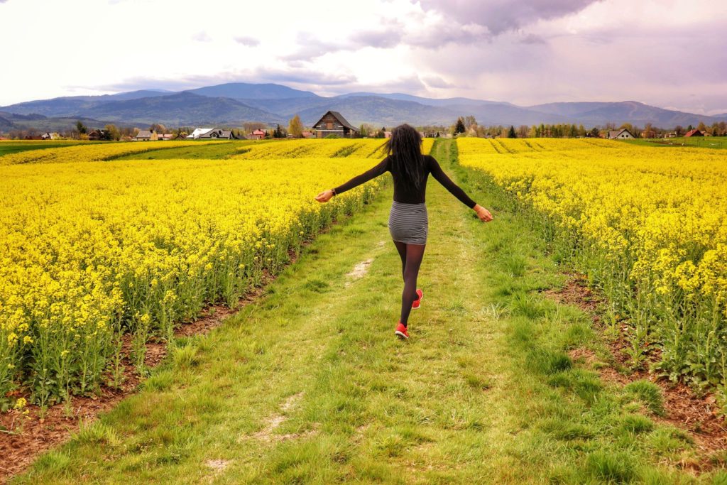 Szczęśliwa kobieta spacerująca między polami rzepaku, w oddali krajobraz górski