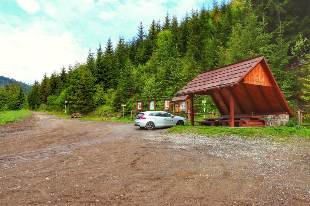 Leśny parking przy czarnym szlaku na Słowiankę z Żabnicy, zaparkowany biały samochód, drewniana wiata