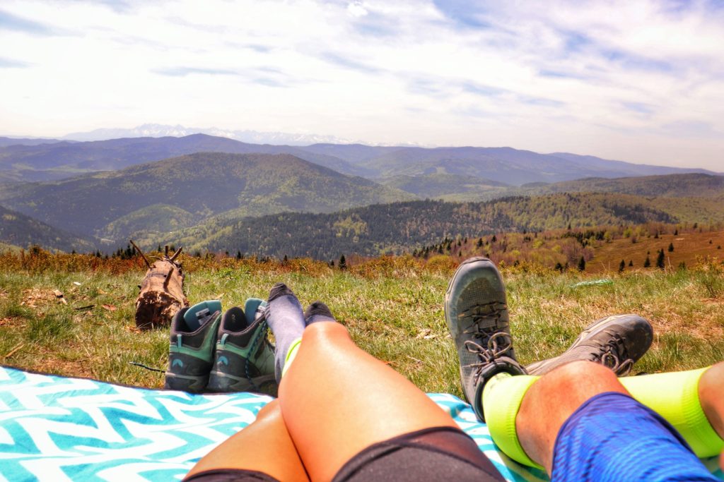 Nogi turystów odpoczywających na kocu na polanie - Polana Stumorgowa, w oddali krajoibraz górski, w tym ośnieżone Tatry