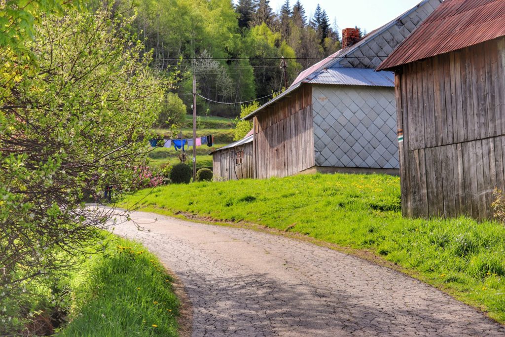 Piękny, majowy dzień w miejscowości Chyszówka, asfaltowa droga, gospodarstwa obok których przechodzi zielony szlak na Mogielicę