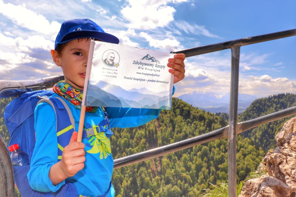 Sokolica z dzieckiem, chłopczyk z flagą akcji zdobywamy szczyty dla hospicjum, w tle krajobraz górski