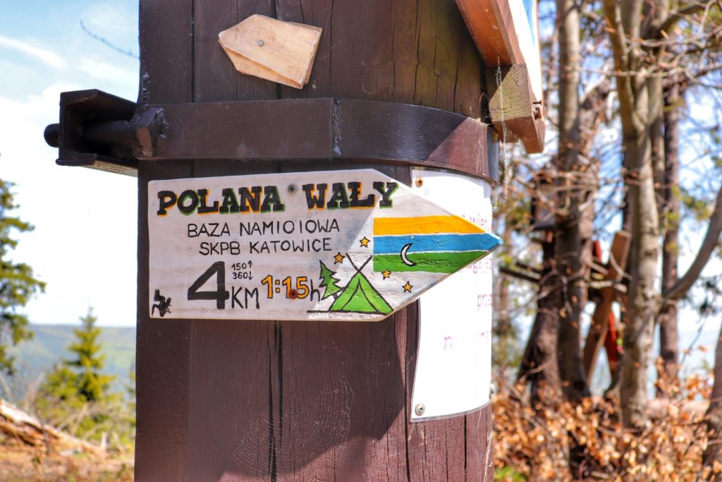 Tabliczka, która jest zawieszona na wieży widokowej na szczycie Mogielica informująca o Polanie Wały oraz znajdującej się na niej Bazie namiotowej SKPB Katowice w odległości 4 km od szczytu Mogielica