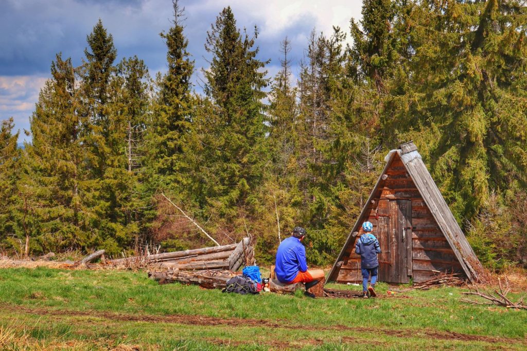 Turyści, tata z dzieckiem odpoczywający przed małym, drewnianym szałasem na Hali Janoszkowej