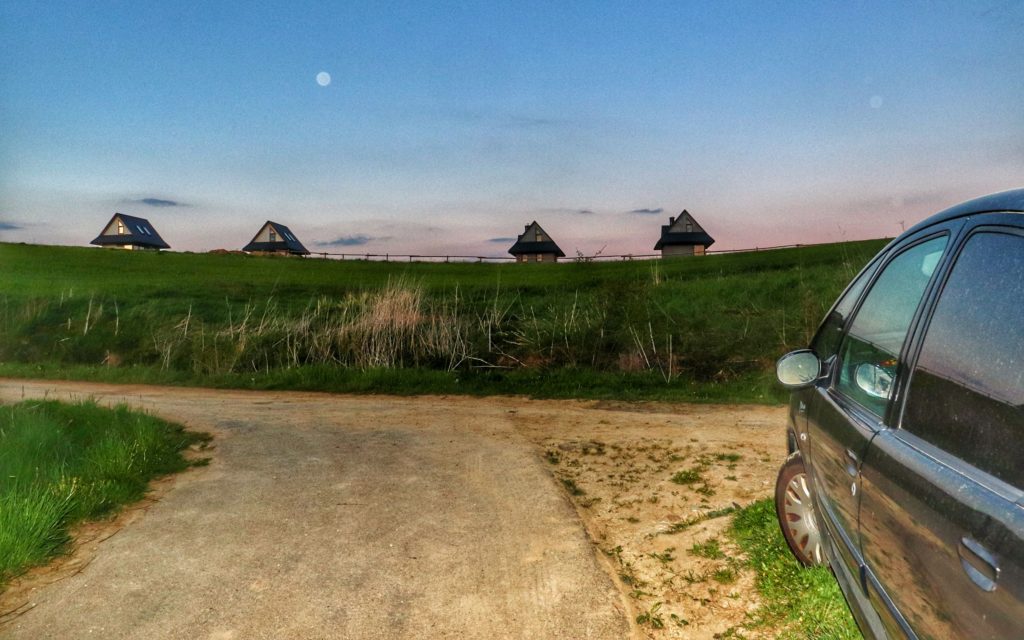 Wieś Dursztyn, późny wieczór, droga między polami, domki, po prawej zaparkowany czarny samochód