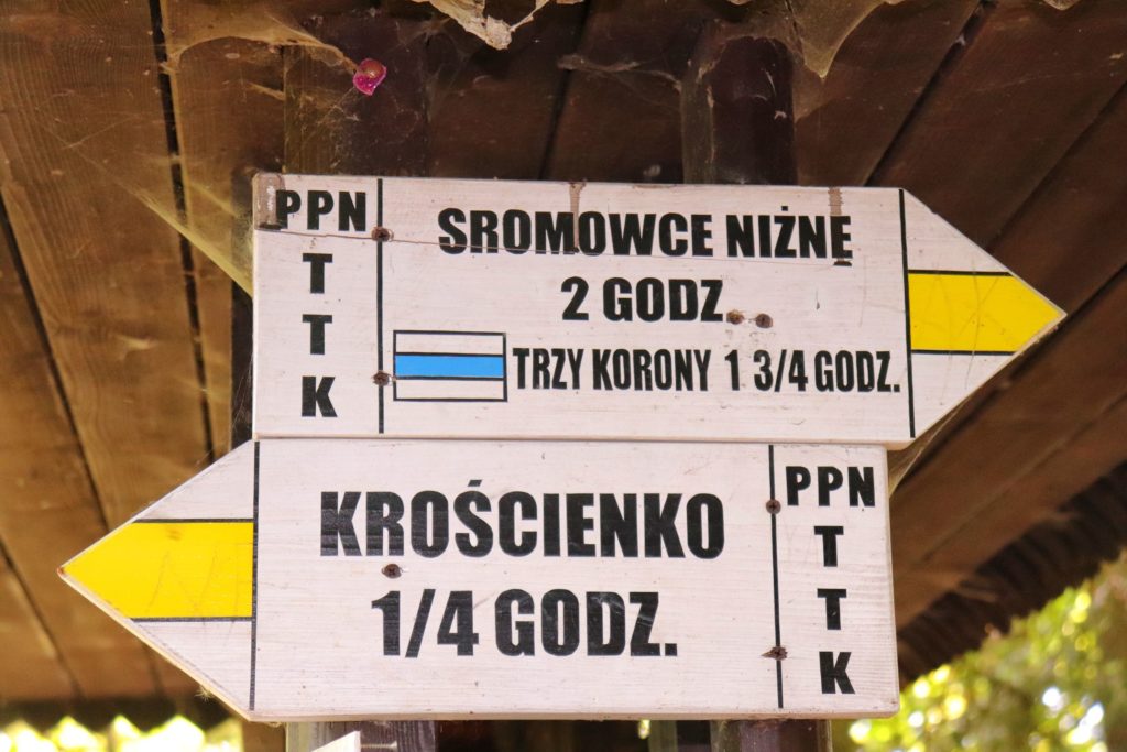 Białe tablice - drogowskazy opisujące żółty szlak w Pienińskim Parku Narodowym między innymi Sromowce Niżne 2 godz. oraz żółto - niebieskie znaki na Trzy Korony