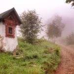 Szeroka, kamienista droga, po lewej stronie kapliczka leśna, zielony szlak na Błatnią, mgliste popołudnie