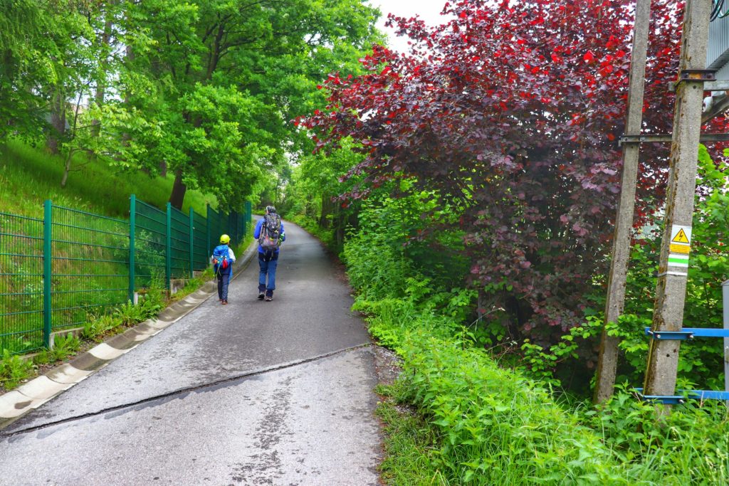 Turysta z dzieckiem idący drogą asfaltową na zielonym szlaku w Brennej prowadzącym do schroniska na Błatniej