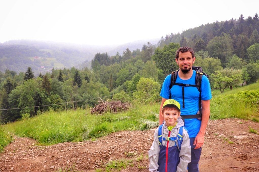 Turysta z dzieckiem, mglisty, czerwcowy dzień na szlaku w Brennej, w oddali zamglone góry