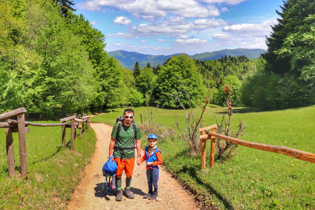 Uśmichnięty turysta z dzieckiem na tle gór w drodze na Przełęcz Szopka, piękny, słoneczny dzień
