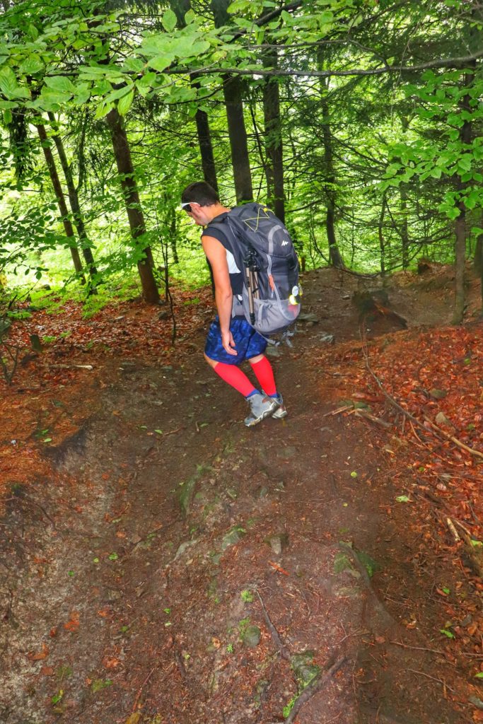 Mężczyzna schodzący stromo w dół, leśną ścieżką w kierunku Źródełka Maryjnego na czerowno - żółtym szlaku na Hrobaczą Łąkę