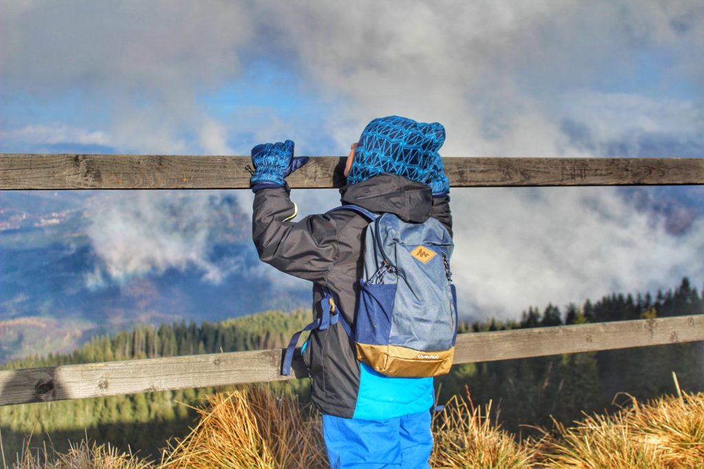 Przełęcz Brona w Babiogórskim Parku Narodowym, dziecko wychylające się za drewniane barierki podziwiając chmury zza których wyłania się widok