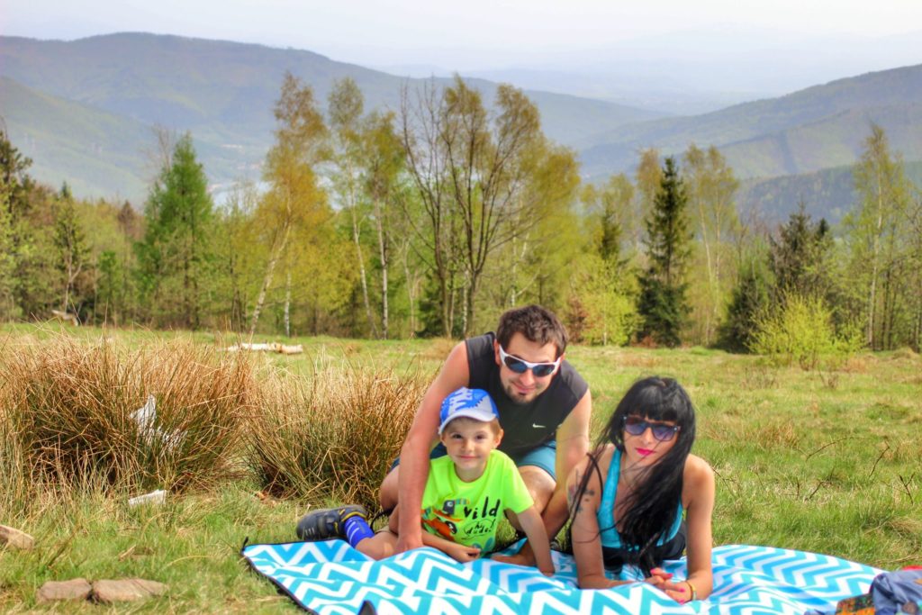 Trzyosobowa, szczęśliwa rodzina odpoczywająca na kocu na Hrobaczej Łące, w tle krajobraz górski