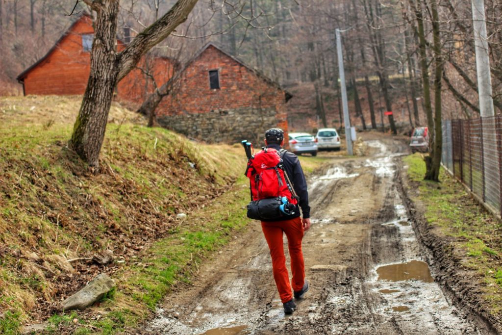Turysta idący czarnym szlakiem z Lipnika, błotnista droga, w oddali domy, zaparkowane samochody