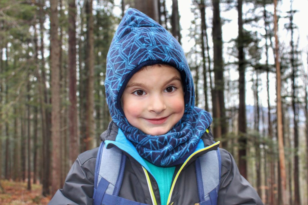 Uśmiechnięte dziecko w zimowym ubraniu na szlaku zielonym w lesie