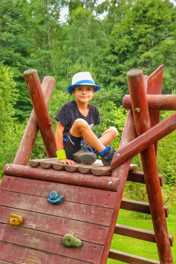 Dziecko siedzące na drewnianej platformie przy ściance wspinaczkowej dla dzieci przy schronisku CYRLA