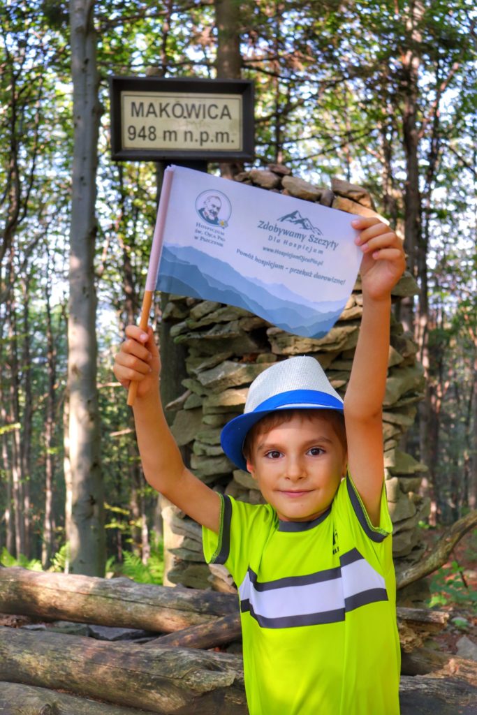 Dziecko trzymające w górze flagę akcji zdobywamy szczyty dla hospicjum na szczycie Makowica w Beskidzie Sądeckim