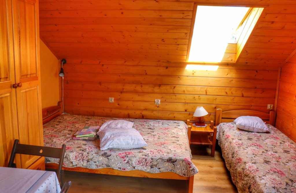 Pokój na poddaszu w schronisku Cyrla, drewniane ściany, łóżka z kwiecistymi narzutami, szafa, stół z krzesłem