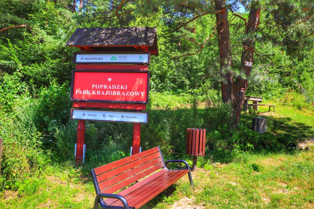Szlak czerwony Rytro, czerwona tablica z napisem Popradzki Park Krajobrazowy, ławka