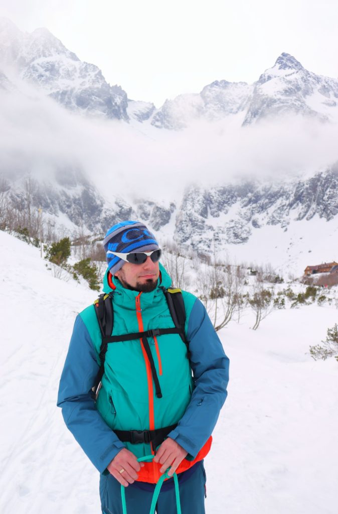 Turysta na tle zaśnieżonych Tatr Wysokich, w tle widać schronisko nad Zielonym Stawem Kieżmarskim