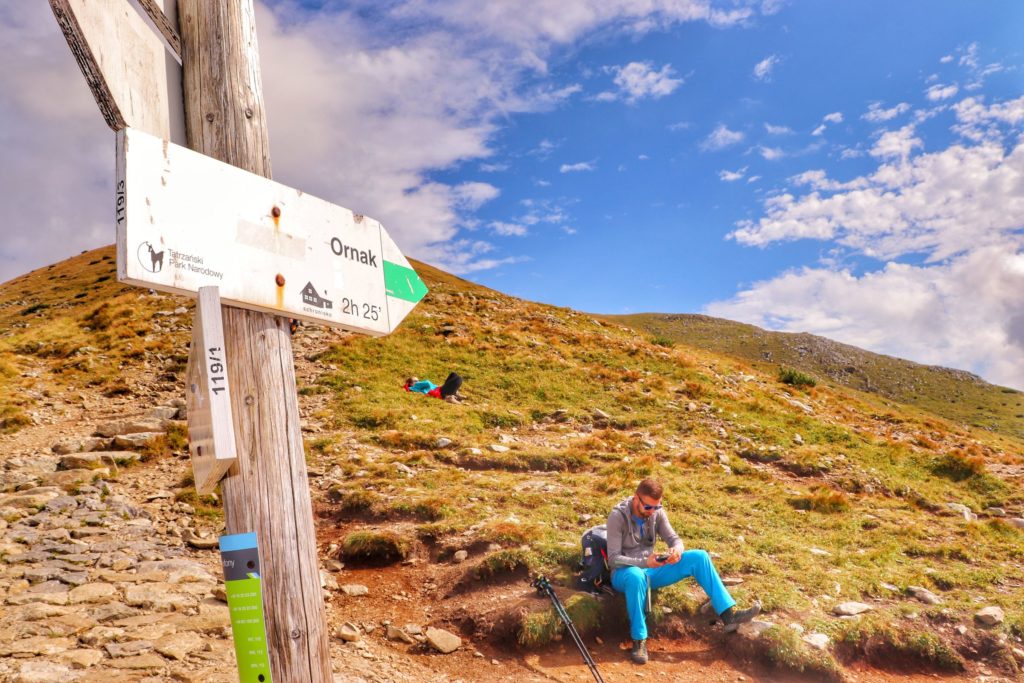 Chuda Przełączka, miejsce skrętu szlaku zielonego do schroniska Ornak, słup z tablicą opisującą zielony szlak, odpoczywający turysta, widoczne podejście w kierunku szczytu Ciemniak