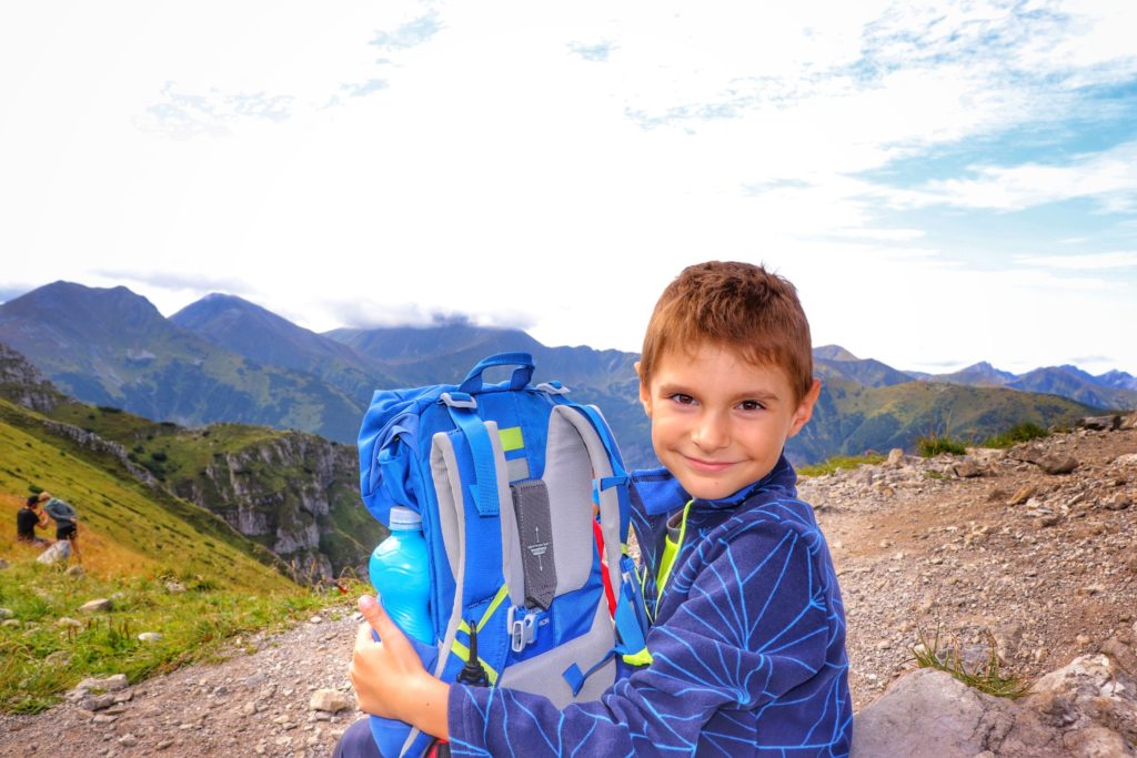 Chuda Przełączka, uśmiechnięte dziecko odpoczywające na czerwonym szlaku na Ciemniak, w tle tatrzańskie szczyty