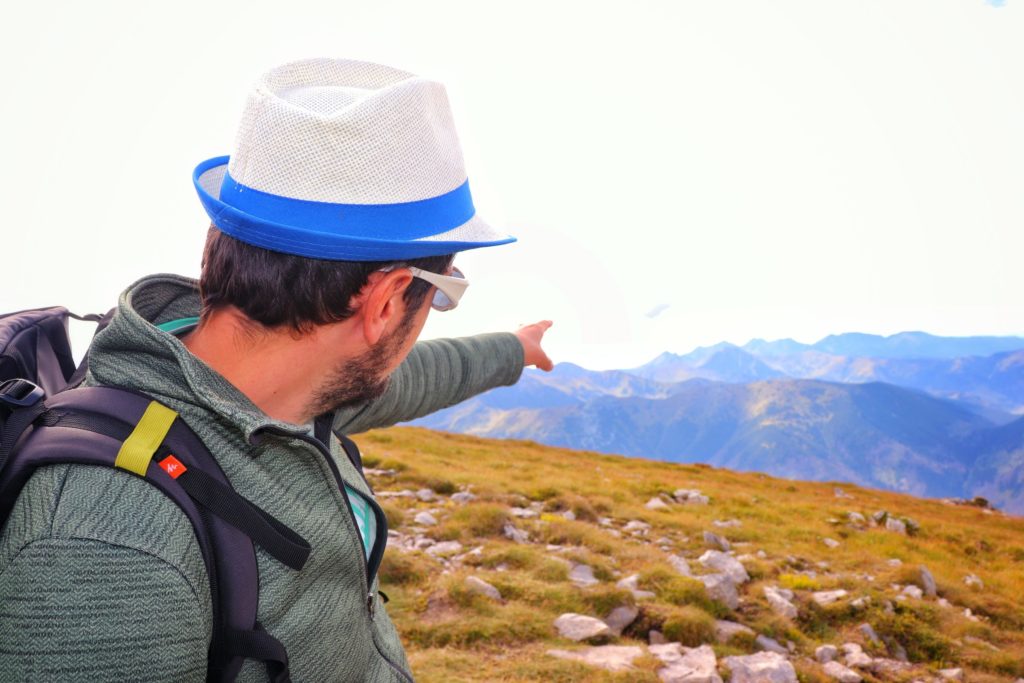 Turysta w kapeluszu wskazujący palcem na tatrzańskie szczyty widoczne ze szczytu Ciemniak