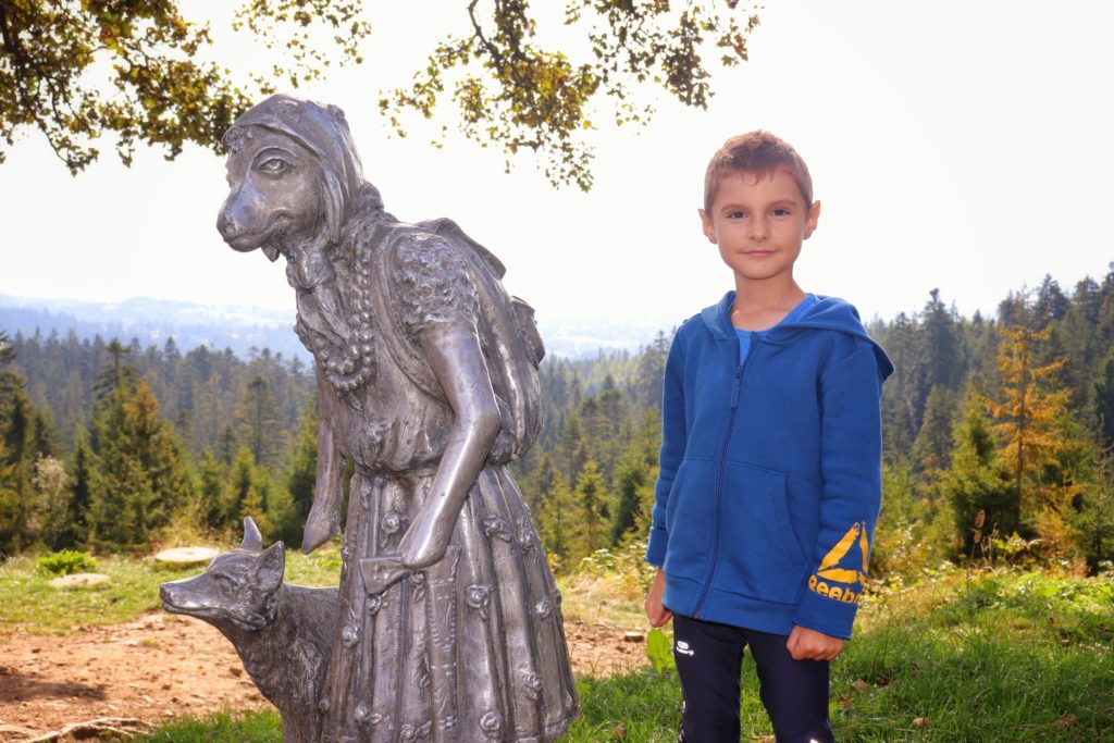 Dziecko stojące obok figurki owcy turystki - Czerwonego Kapturka z wilkiem na Łapsowej Polanie w Gorcach, owczy szlak Nowego Targu