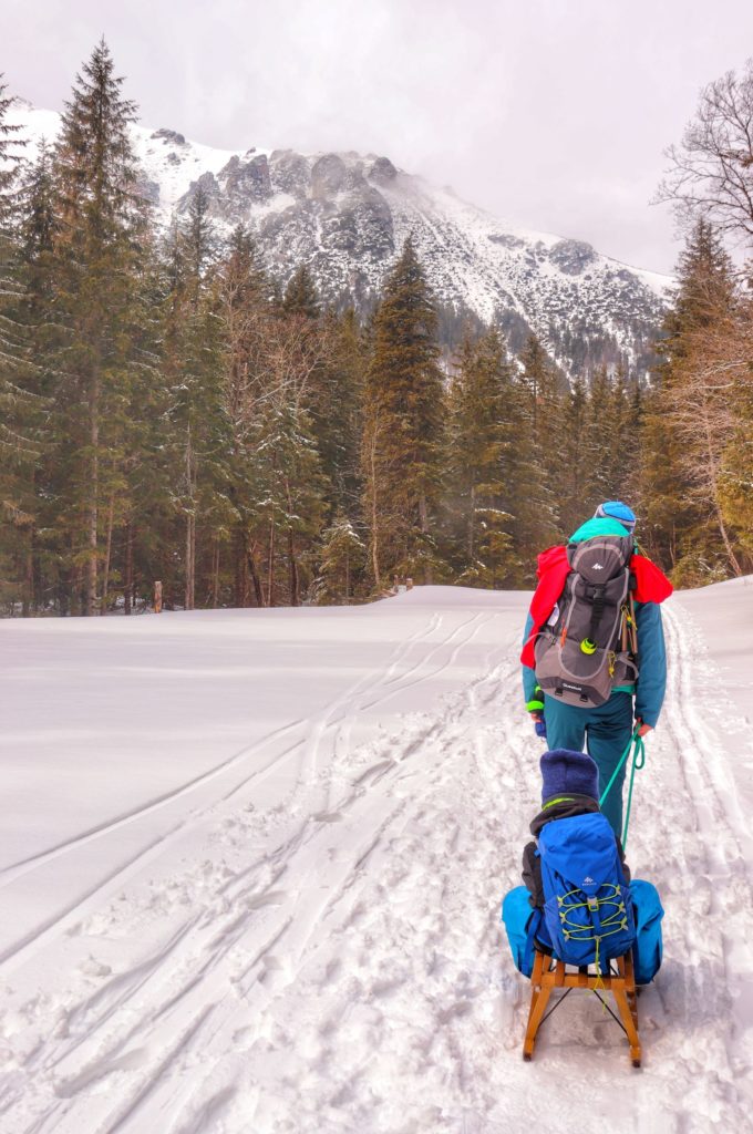 Mężczyzna ciągnący dziecko siedzące na drewnianych sankach, Tatry Słowackie