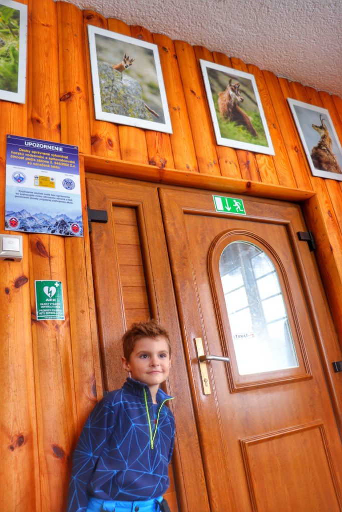 Mały turysta w chacie przy Zielonym Stawie w słowackich Tatrach opierający się o wykończoną drewnem ścianę, nad drzwiami wiszą zdjęcia kozic