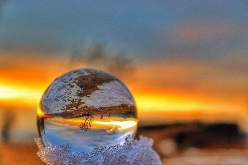 Szklana kula leżąca w śniegu, w której odbija się Hala Jaworowa o zachodzie słońca, niebiesko - pomarańczowe niebo