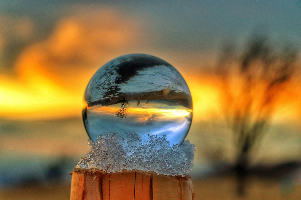 Szklana kula ustawiona na drewnianym słupie, opatulona śniegiem, w której odbija się Hala Jaworowa (Brenna), drzewo oraz niebo zakolorowane przez zachodzące słońce