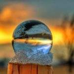 Szklana kula ustawiona na drewnianym słupie, opatulona śniegiem, w której odbija się Hala Jaworowa (Brenna), drzewo oraz niebo zakolorowane przez zachodzące słońce