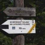 Łapsowa w Gorcach, biała tabliczka w krztsałcie strzałki (drogowskaz) informujący, że do Schroniska Koliby na Łapsowej Polanie jest 15 minut szlakiem czarnym