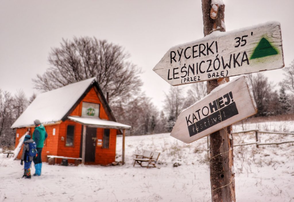 Białe tabliczki, zielony szlak bazowy, Studencka Baza Namiotowa Przyszłop Potócki, w tle turysta z dzieckiem, zaśnieżona drewniana chatka
