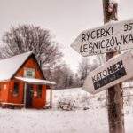 Białe tabliczki, zielony szlak bazowy, Studencka Baza Namiotowa Przyszłop Potócki, w tle turysta z dzieckiem, zaśnieżona drewniana chatka
