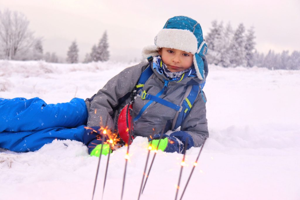 Dziecko leżące na śniegu na Hali na Muńczole podziwiające zimne ognie