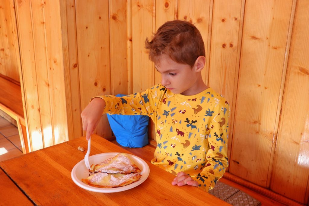 Dziecko siedząca przy drewnianym stole w schronisku pod Łabskim Szczytem, jedzące naleśniki z serem